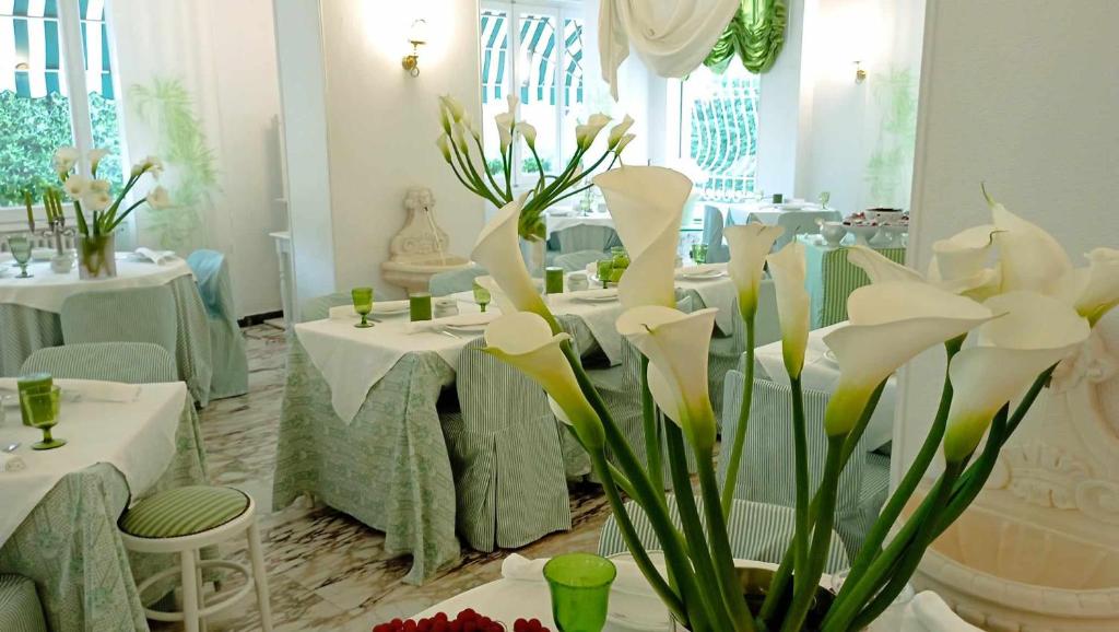 uma sala de jantar com mesas brancas e flores brancas em Eveline Portosole Hotel em Sanremo
