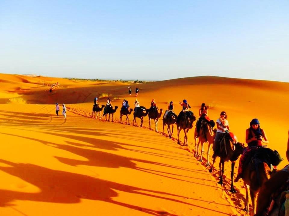 a group of people riding horses in the desert at Enjoy Moda Camp Merzouga tours- Camel sunset sunrise Quad Sunboarding ATV in Merzouga