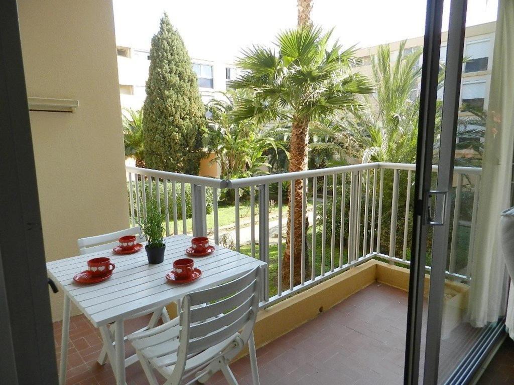 une table et des chaises blanches sur un balcon avec des palmiers dans l'établissement Appartement avec Piscine et Tennis, 2 Ch, Terrasse, Parking, WiFi - Proche Plage, Le Lavandou - FR-1-251-794, au Lavandou