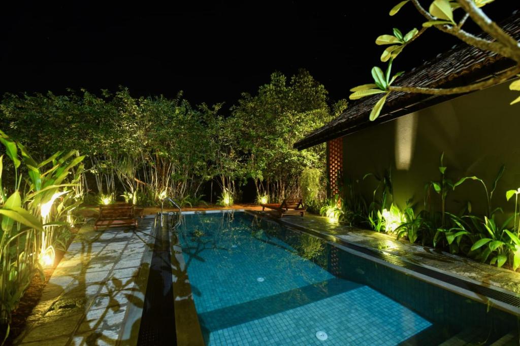 a swimming pool in a garden at night at Pivithuru River Cabanas in Hikkaduwa