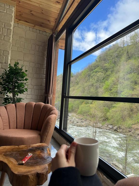 a person holding a cup of coffee in front of a window at Karadeniz River Palace in Çamlıhemşin