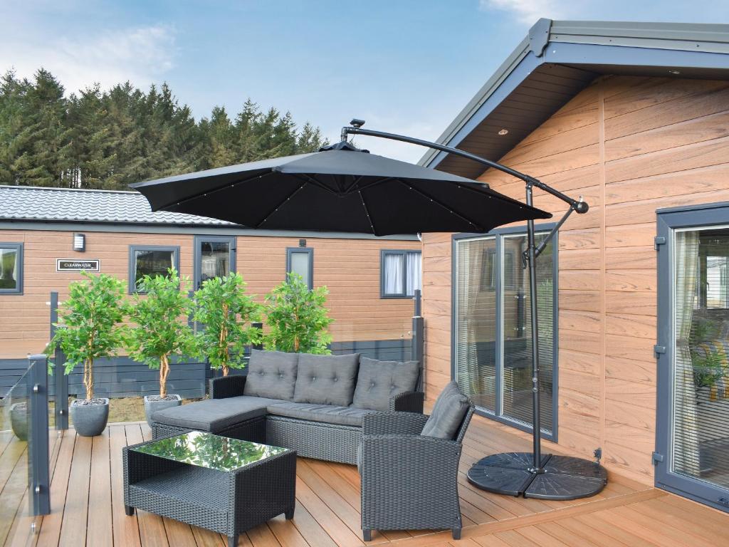 Plumbland的住宿－Beaumont Lodge，平台上设有带沙发和遮阳伞的天井。