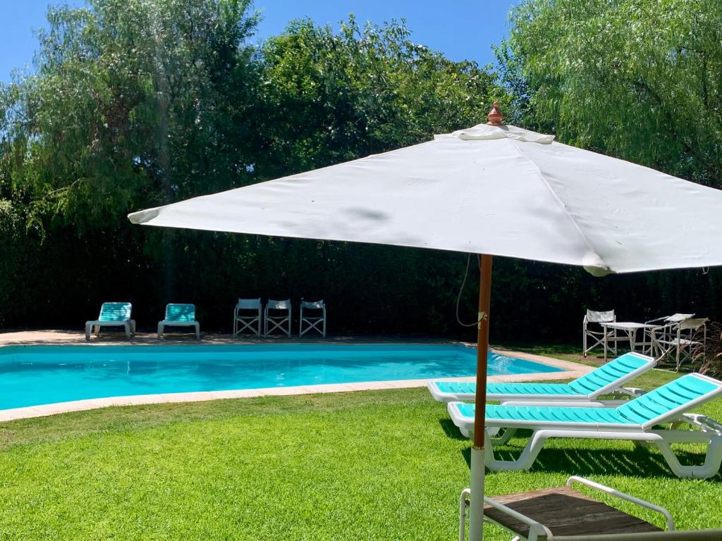 ラ・クンブレにあるHostería La Viñaのスイミングプールの横の白い傘と椅子