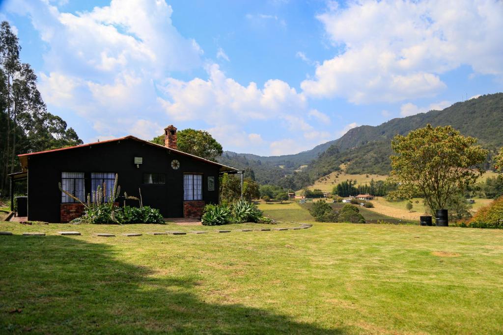 una pequeña casa en un campo con montañas en el fondo en Casa de Campo en la Montaña Negra-Subachoque, en Subachoque