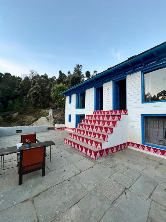 a patio with a table and a building with red chairs at Idyllic Haven Heritage, Jageshwar in Jageshwar