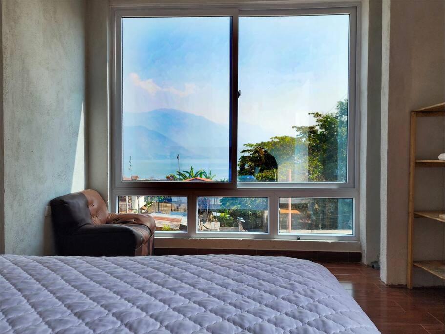 a bedroom with a large window with a chair and a bed at Habitación#1 Casa Rosita a metros del Lago in San Pedro La Laguna