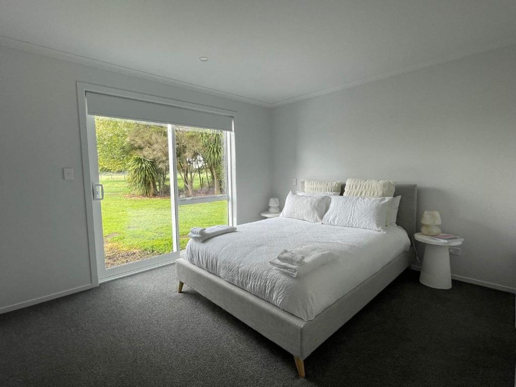 a white bedroom with a bed and a large window at Modern and new house in Taupiri
