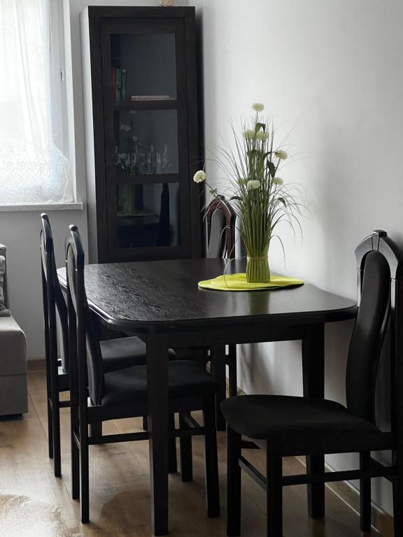 Apartament dla Ciebie في كنتشين: طاولة طعام سوداء مع كراسي و إناء من الزهور