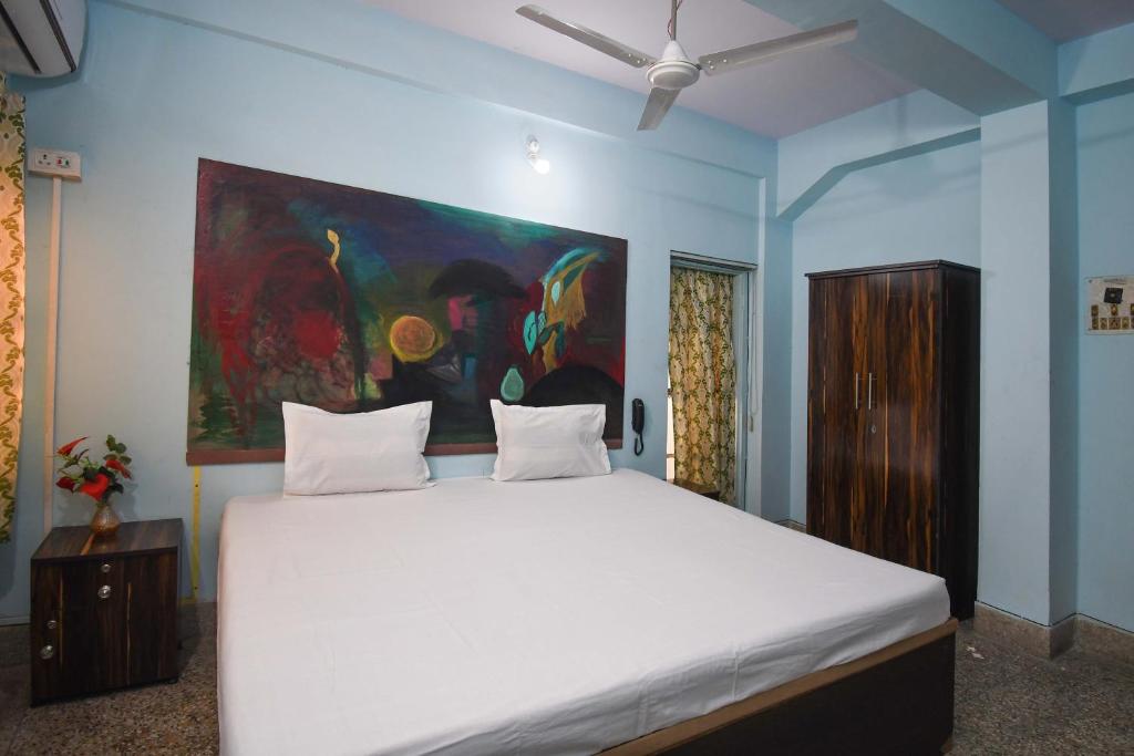 a bedroom with a white bed with a painting on the wall at OYO Blue Cherry Guest House in Ballygunge