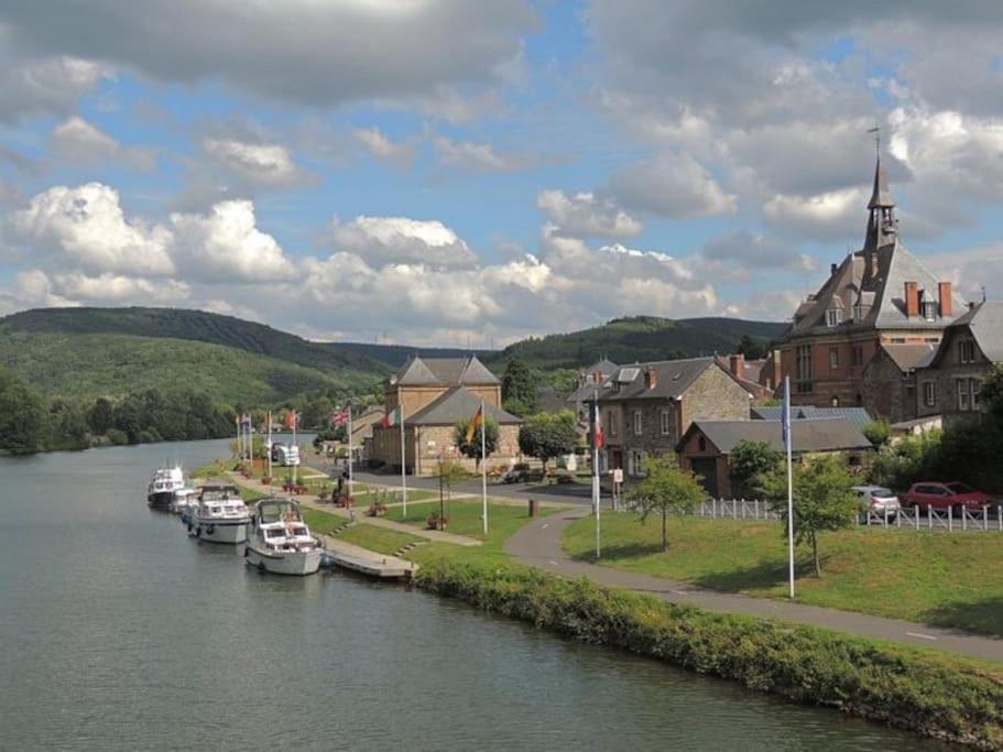 a river with boats docked in a town with a church at Logement en bord de Meuse « La Jolie Rose » in Haybes
