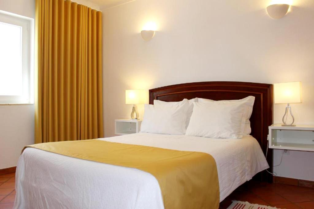 a bedroom with a large bed with yellow curtains at Guest House - Duna Parque Group in Vila Nova de Milfontes