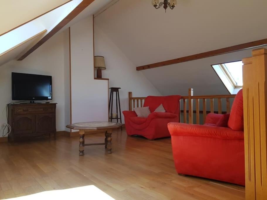 ein Wohnzimmer mit 2 roten Stühlen und einem TV in der Unterkunft Gîte les cocottes in Le Chesne