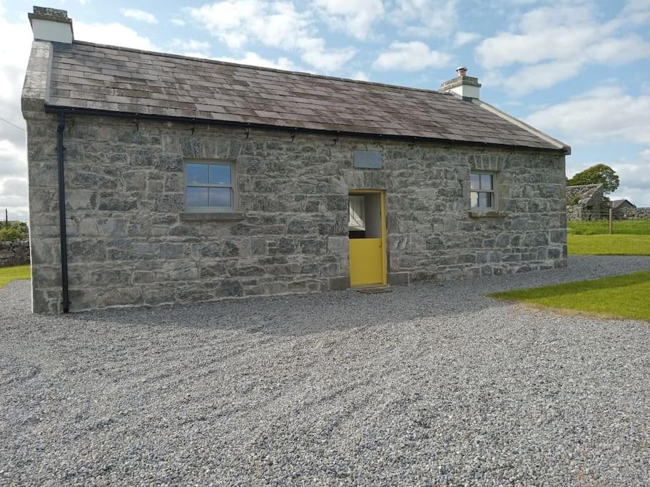 a stone building with a yellow door on a gravel driveway at St Johns old Schoolhouse in Lecarrow