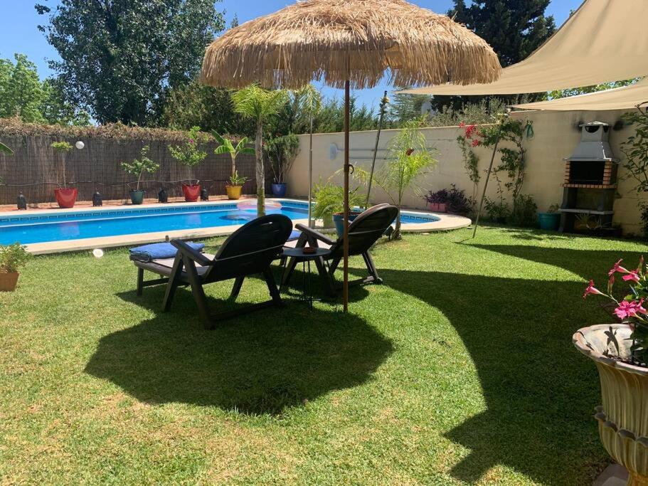 een tafel en stoelen onder een parasol naast een zwembad bij Casa Bignonia in Salteras