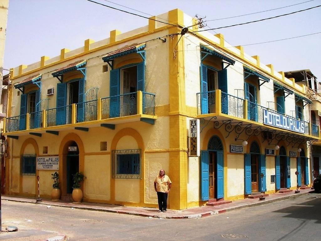 a man standing in front of a yellow building at HOTEL DU PALAIS in Saint-Louis