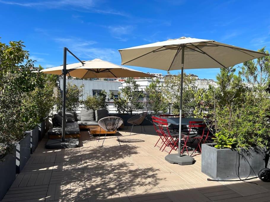 eine Terrasse mit 2 Sonnenschirmen, einem Tisch und Stühlen in der Unterkunft Duplex terrasses vue la Défense in Suresnes