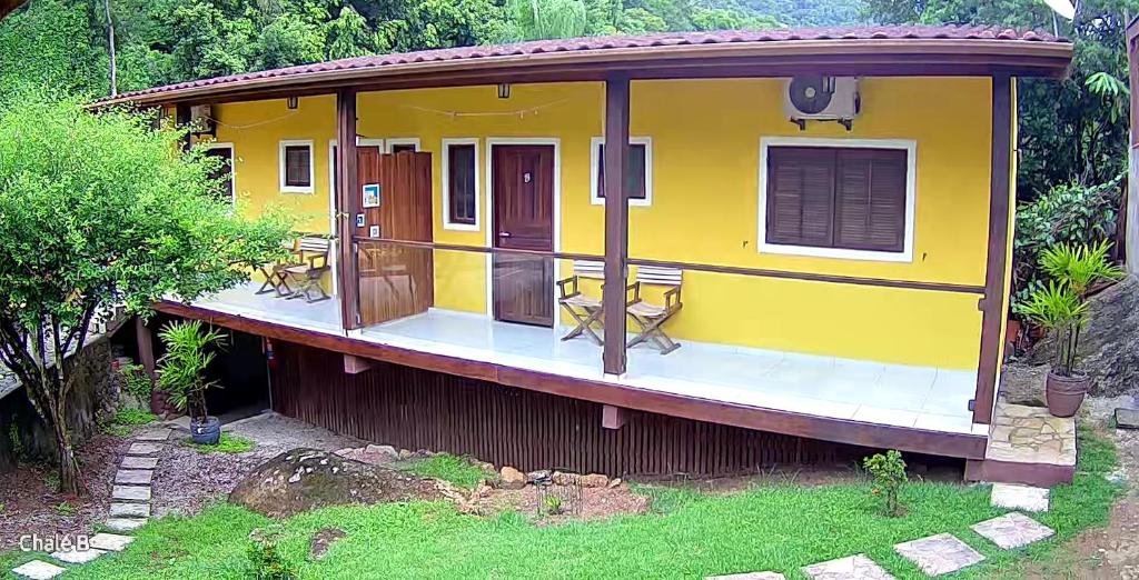 a yellow house with chairs on the deck at Chalés Azuleto - Ilhabela in Ilhabela