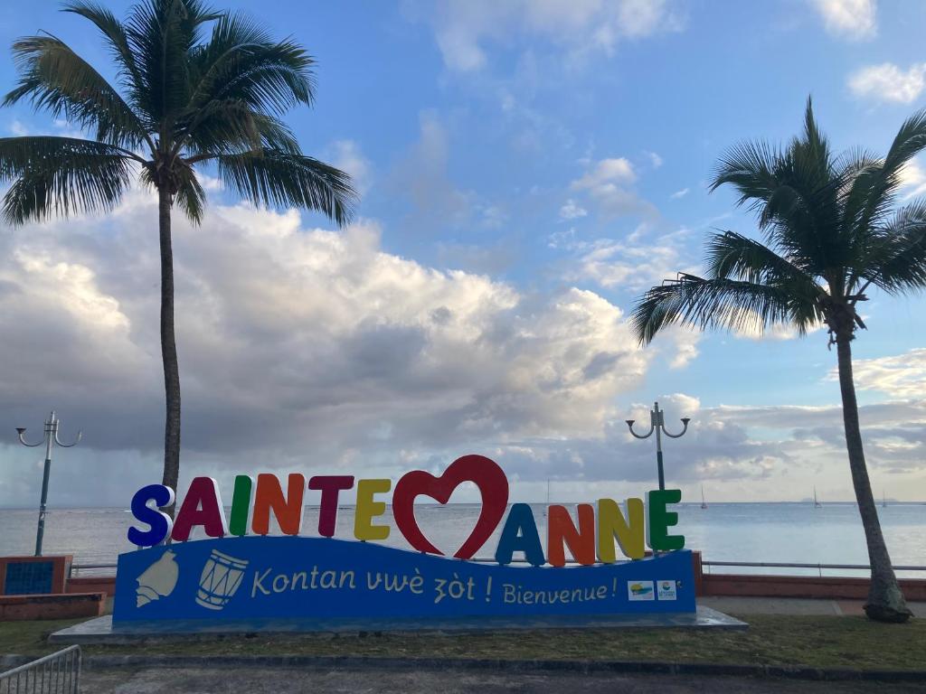 a sign at the beach with two palm trees at Les pieds dans l'eau face au lagon - Le Bel Instant in Sainte-Anne