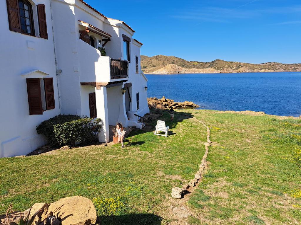 una persona in piedi accanto a un edificio vicino all'acqua di Casa con jardin ,vistas al mar y atardecer en Playas de Fornells a Es Mercadal