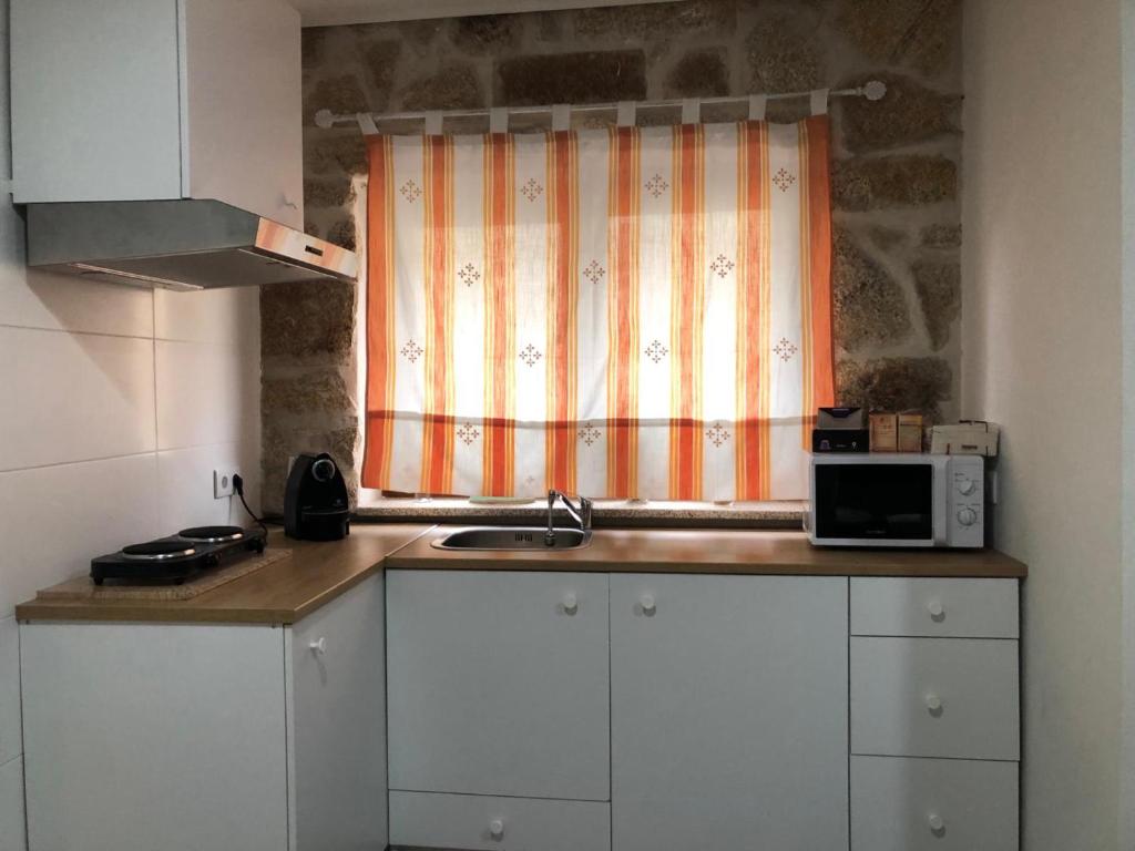 eine Küche mit einer Spüle und ein Fenster mit einer Mikrowelle in der Unterkunft Covo Residence - Casa Santiago in Vila Nova de Paiva