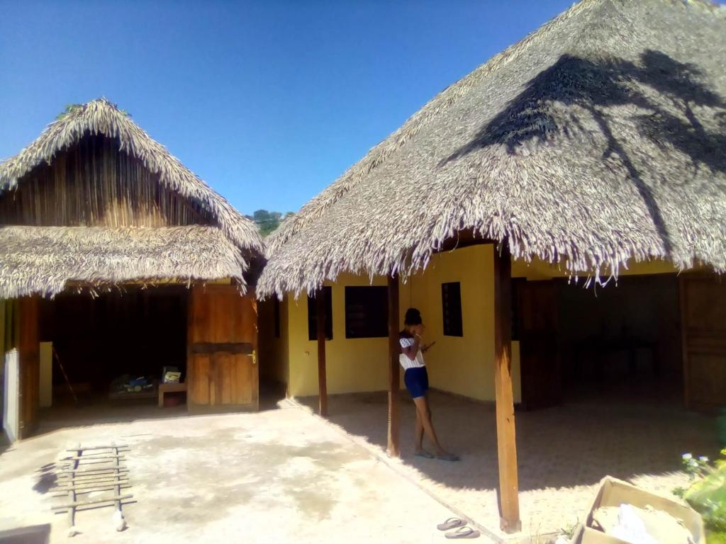 une femme debout devant un bâtiment avec deux cabanes dans l'établissement Meva, à Hell-Ville