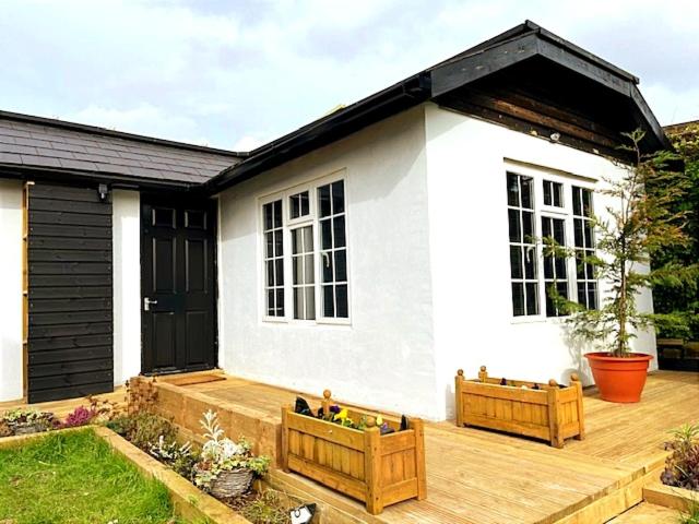 Pine Cottage في Streatham: منزل أبيض صغير مع شرفة خشبية