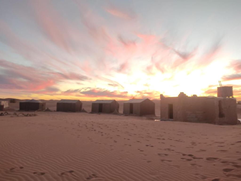 una puesta de sol en el desierto con edificios en la arena en Wüstencamp in Erg Chegaga, en Mhamid