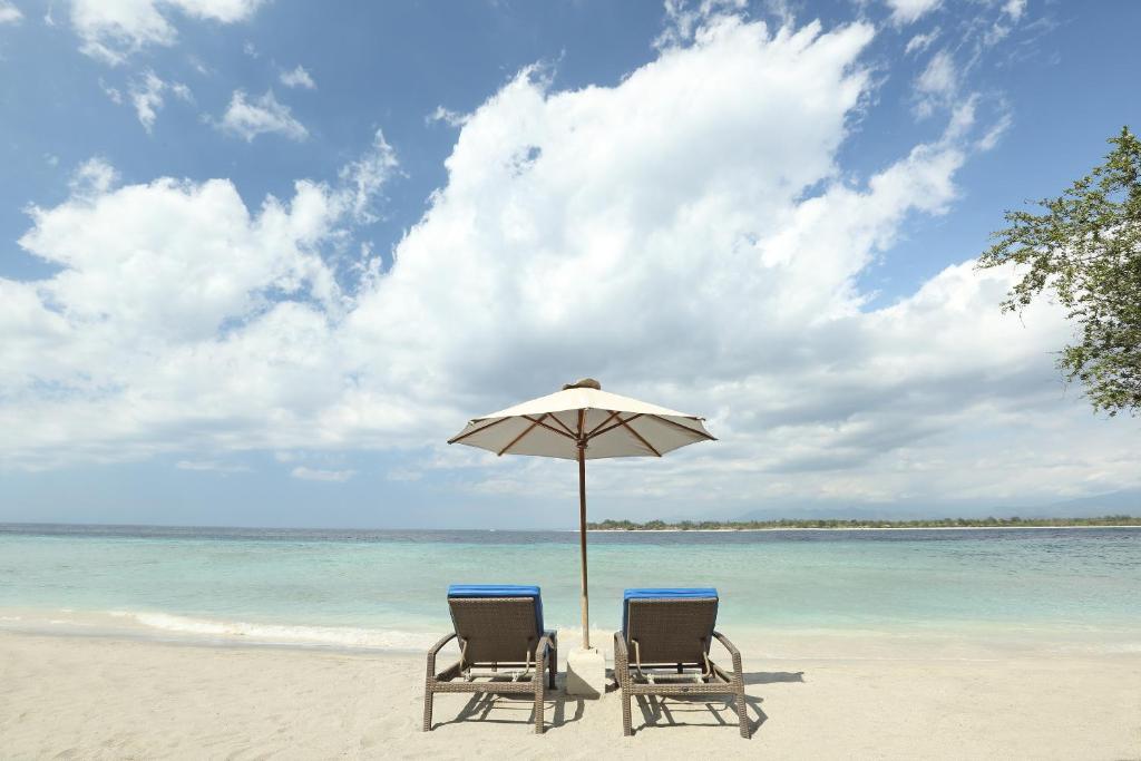 two chairs and an umbrella on a beach at Vamana Resort - CHSE Certified in Gili Trawangan
