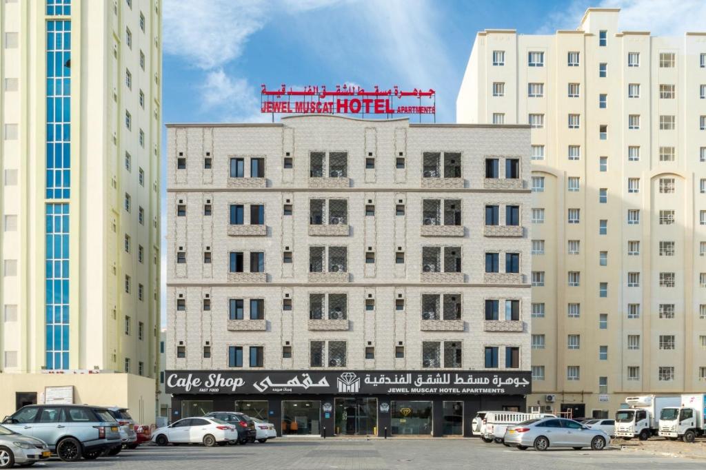 a large white building with cars parked in a parking lot at جوهرة مسقط للشقق الفندقية in Ma‘ābīlah