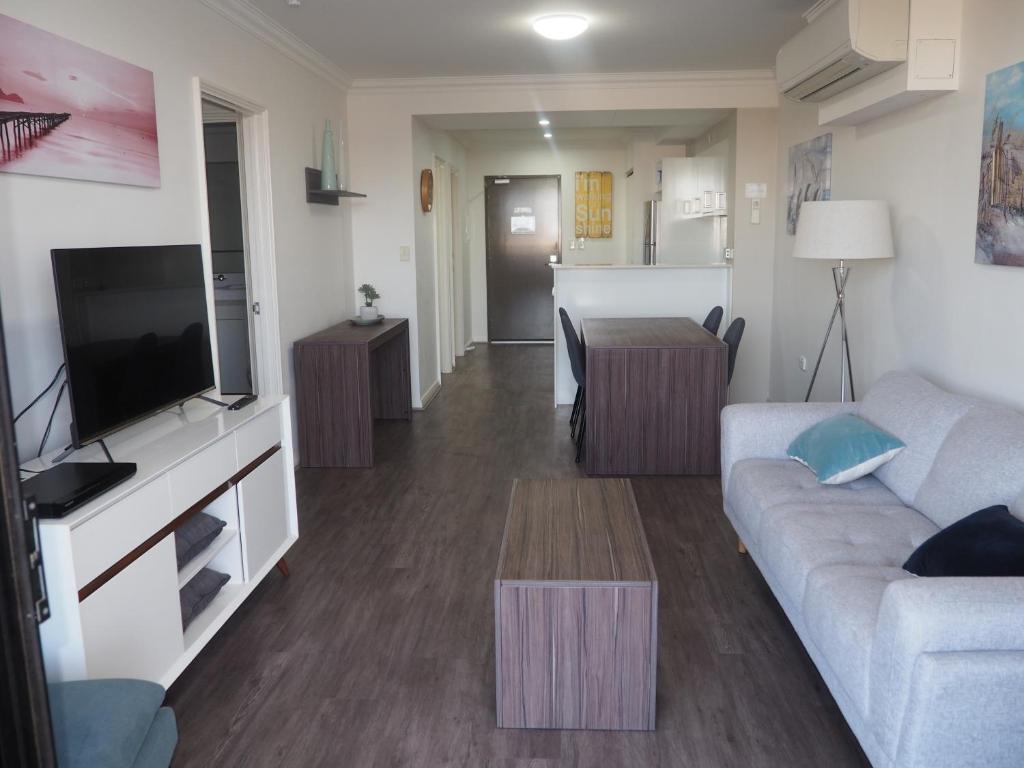 a living room with a couch and a tv and a table at Lovely 2 Bedroom Serviced Apartment & Free Parking in Mandurah