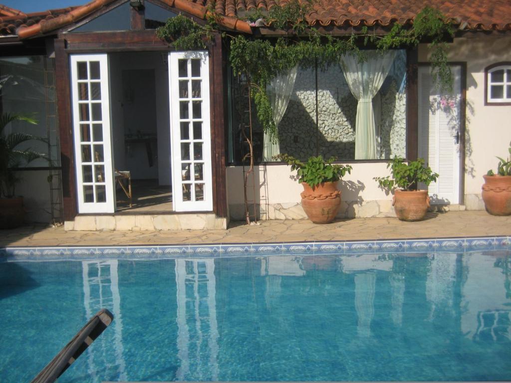 a swimming pool in front of a house with potted plants at Guest House Green Garden in Búzios