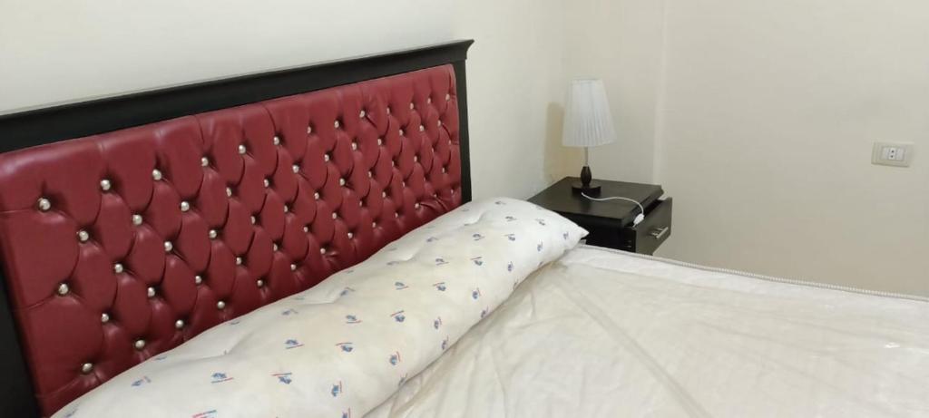 a bed with a red headboard next to a lamp at For Family شاليه in Suez