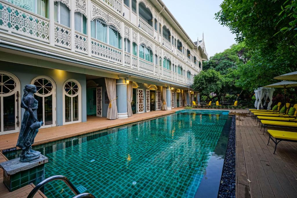 A long tiled pool runs beside the ornate hotel building and a row of loungers.