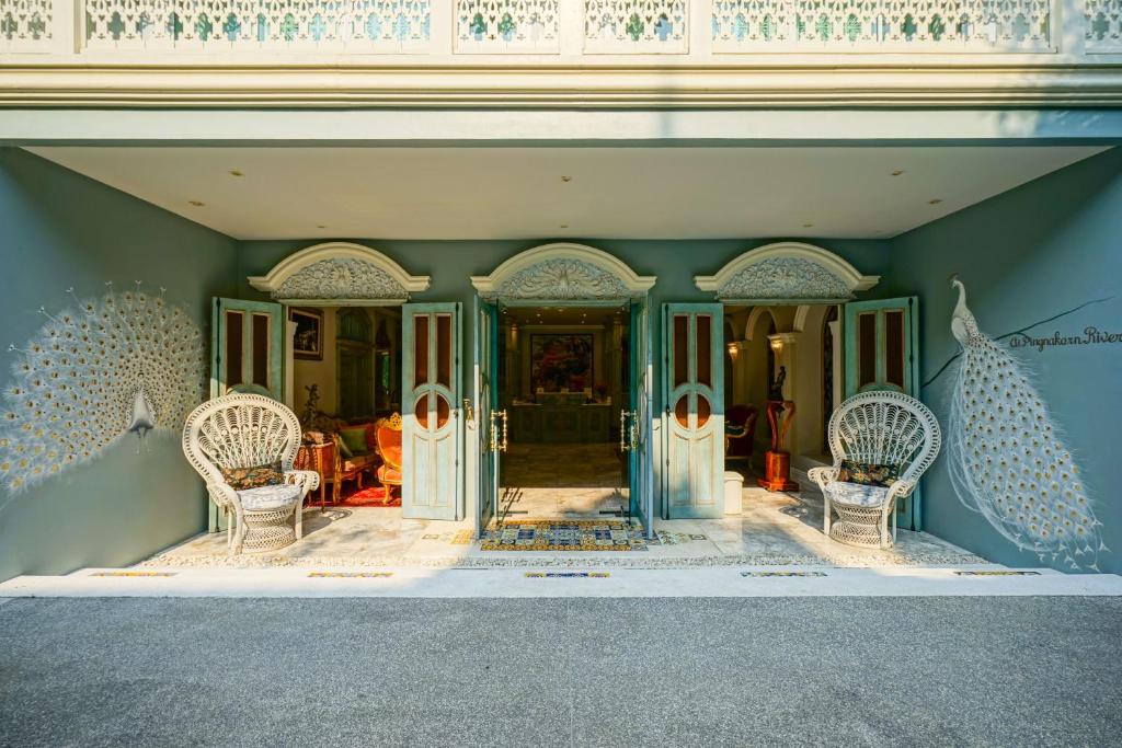The entrance opens onto a decorative blue-green façade flanked by two white wicker chairs and peacock artwork.