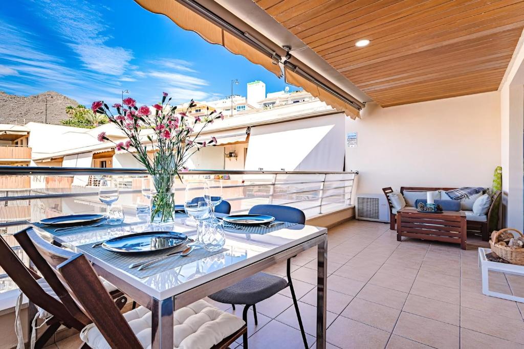 een tafel met stoelen en een vaas met bloemen op een patio bij Los Gigantes Cliffs Sapphire Ocean View in Puerto de Santiago
