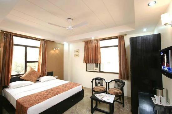 Hotel Jeniffer Inn في نيودلهي: غرفة نوم بها سرير وتلفزيون و نافذتين