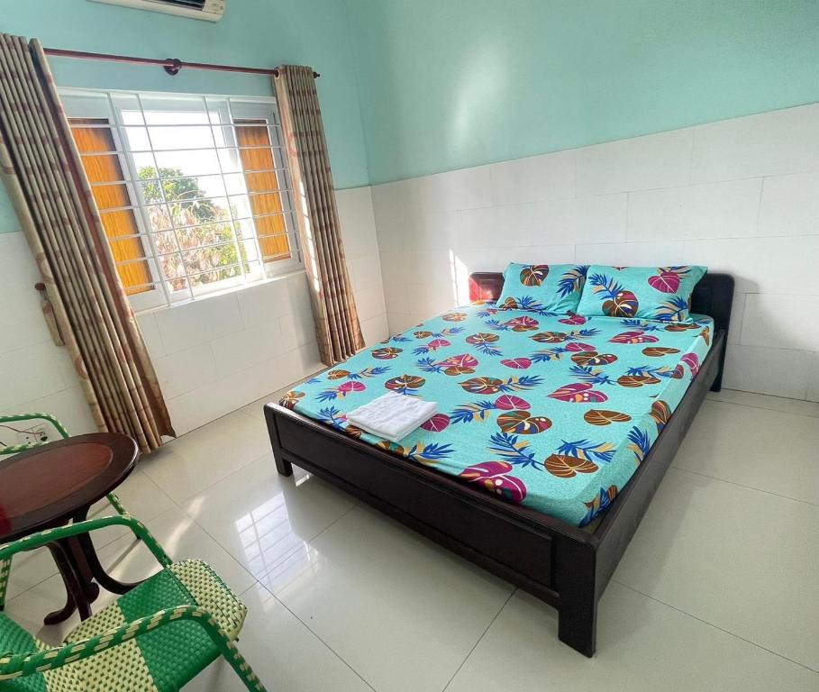 a bedroom with a bed with a blue comforter and a window at Nhà nghỉ Vân Châu-Cát Tường in Ấp Chô Bên
