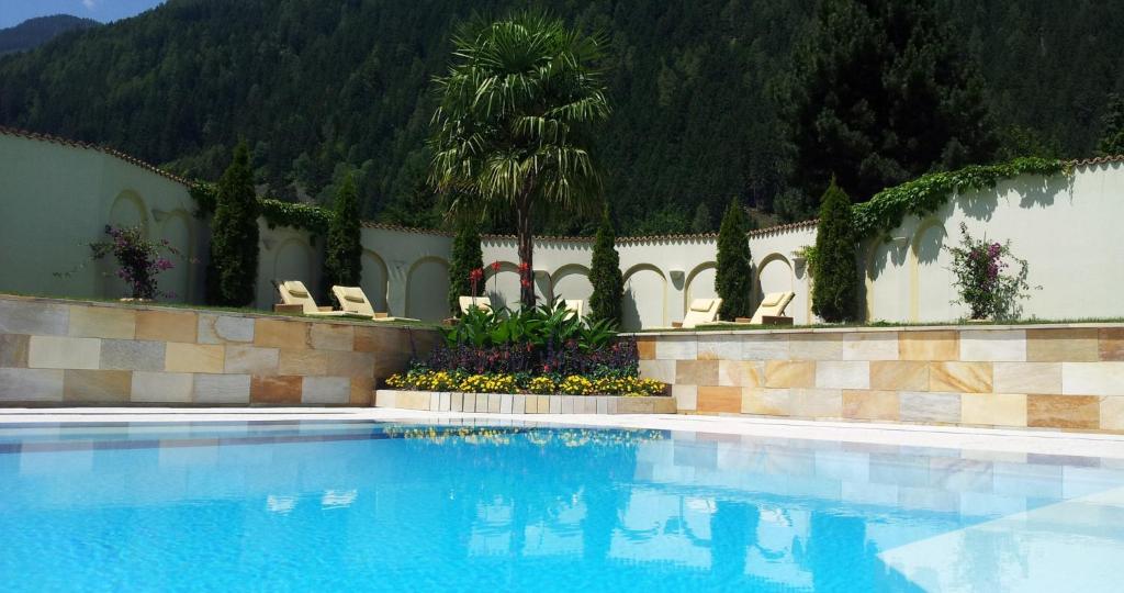a large swimming pool with chairs and trees and a mountain at Forster's Naturresort in Neustift im Stubaital
