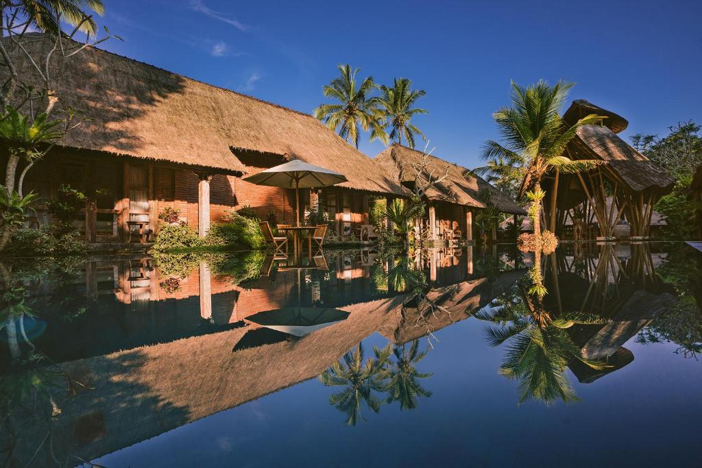 a resort with a reflection in the water at De Umah Bali Eco Tradi Home in Bangli