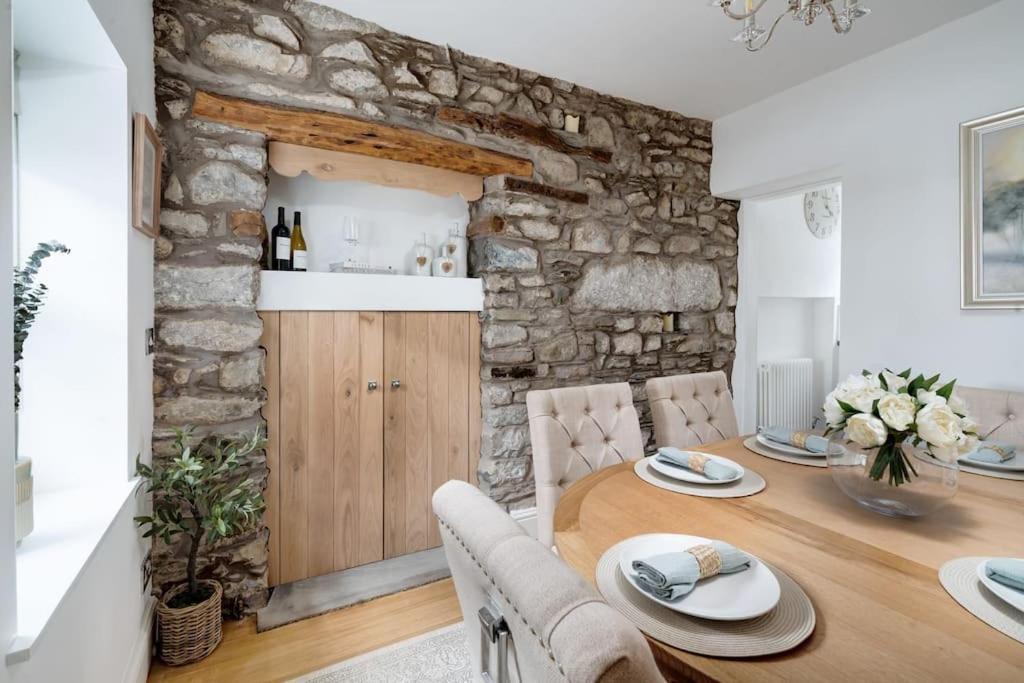 a dining room with a table and a stone wall at Wharton Cottage, Lake District Retreat in Cartmel
