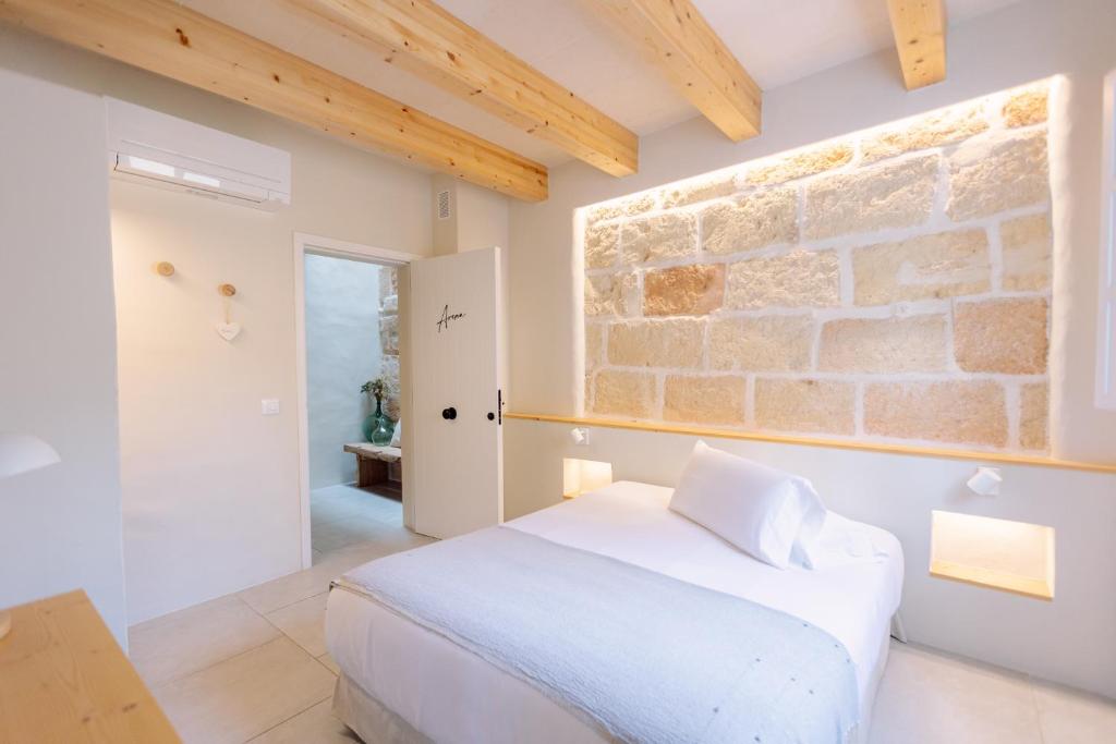 a bedroom with a white bed and a stone wall at Marosi Boutique Hotel in Ciutadella