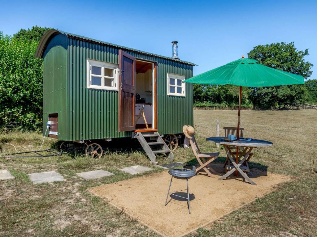a green tiny house with a table and an umbrella at 1 Bed in Horam 88900 in Horam
