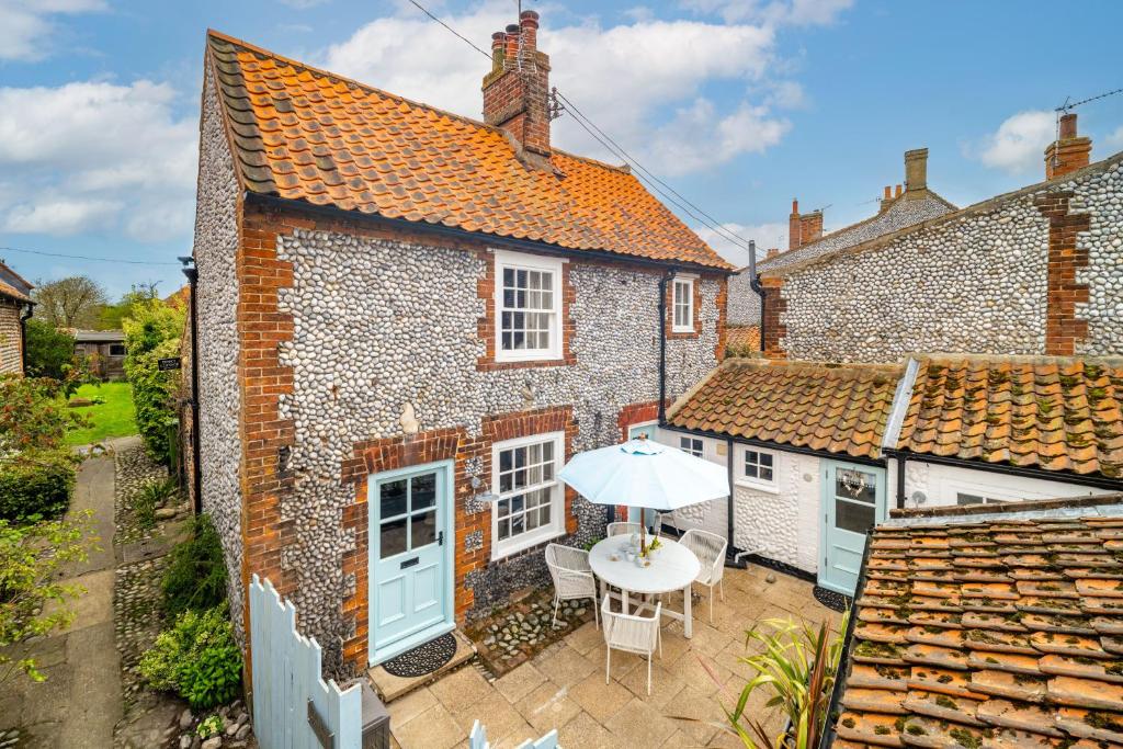 an old brick house with a table and an umbrella at Yew Tree Cottage in Blakeney