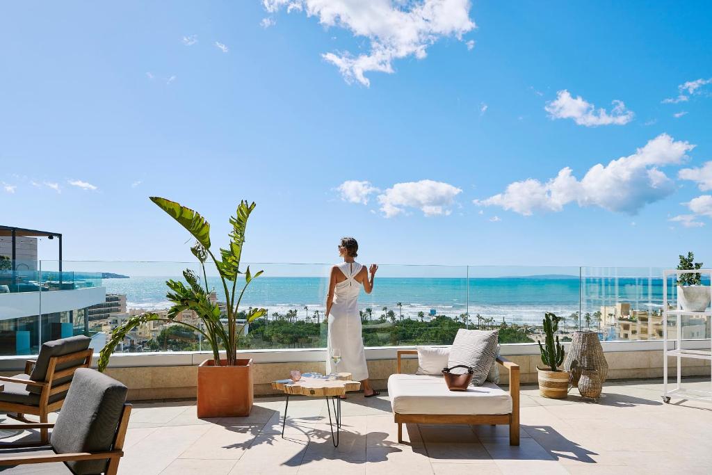 a woman in a white dress standing on a balcony with the ocean at Iberostar Selection Llaut Palma- Adults Only in Playa de Palma