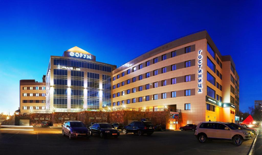 a large building with cars parked in a parking lot at Hotel Forum in Magnitogorsk