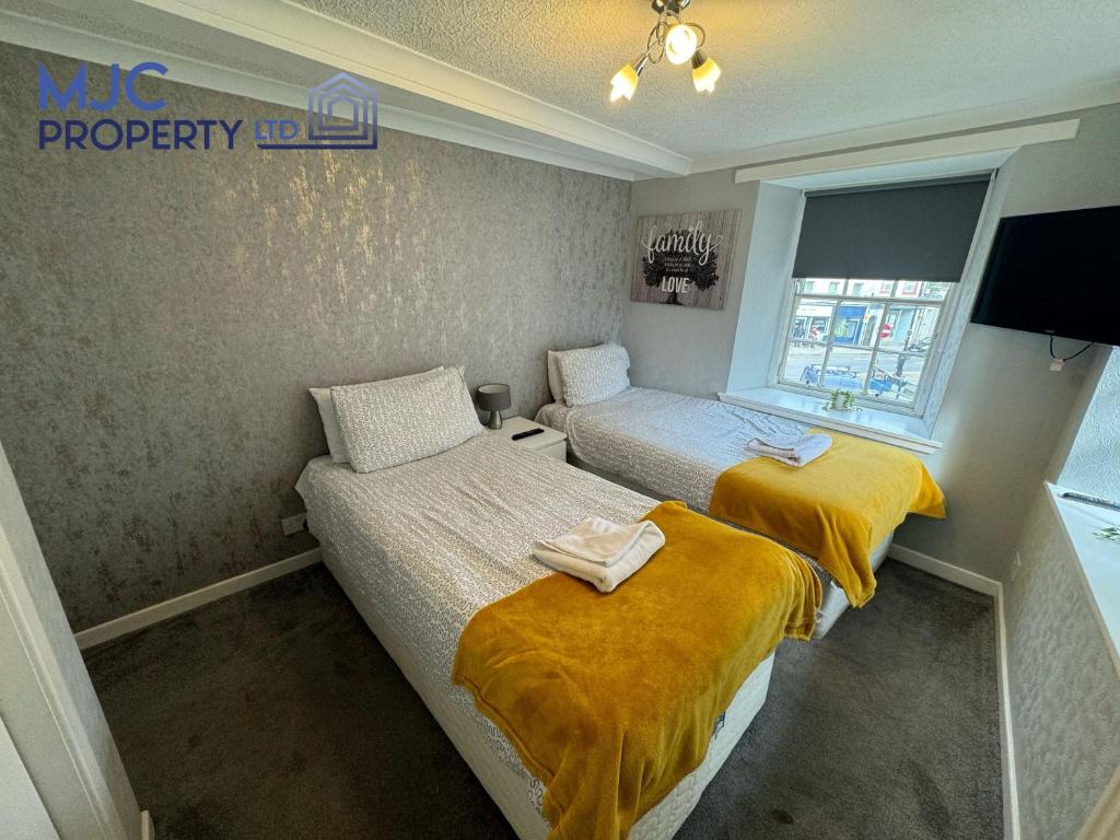 2 Betten in einem kleinen Zimmer mit gelben Decken in der Unterkunft Towerknowe in Hawick