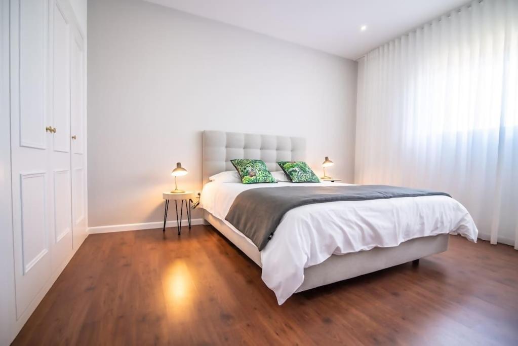 a white bedroom with a large bed with green pillows at Cozy Sea View Apartment near City and Airport in Ponta Delgada