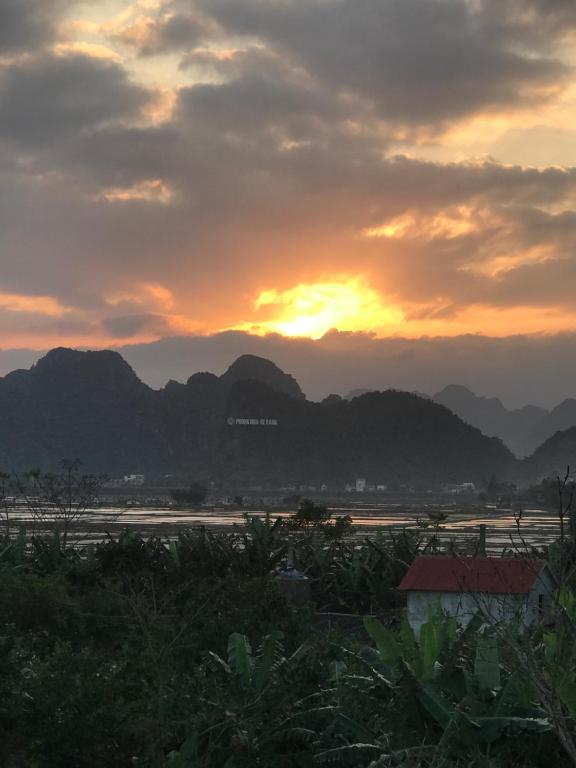 einen Sonnenuntergang mit Bergen im Hintergrund und einem Wasserkörper in der Unterkunft Happy field homestay in Phong Nha