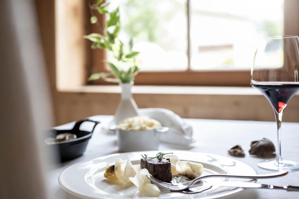 a table with a plate of food and a glass of wine at Adler Spa Resort Dolomiti in Ortisei