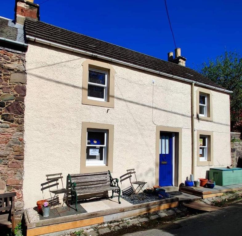Abernethy的住宿－Pitcaithly Cottage，白色的房子,有长凳和蓝色的门